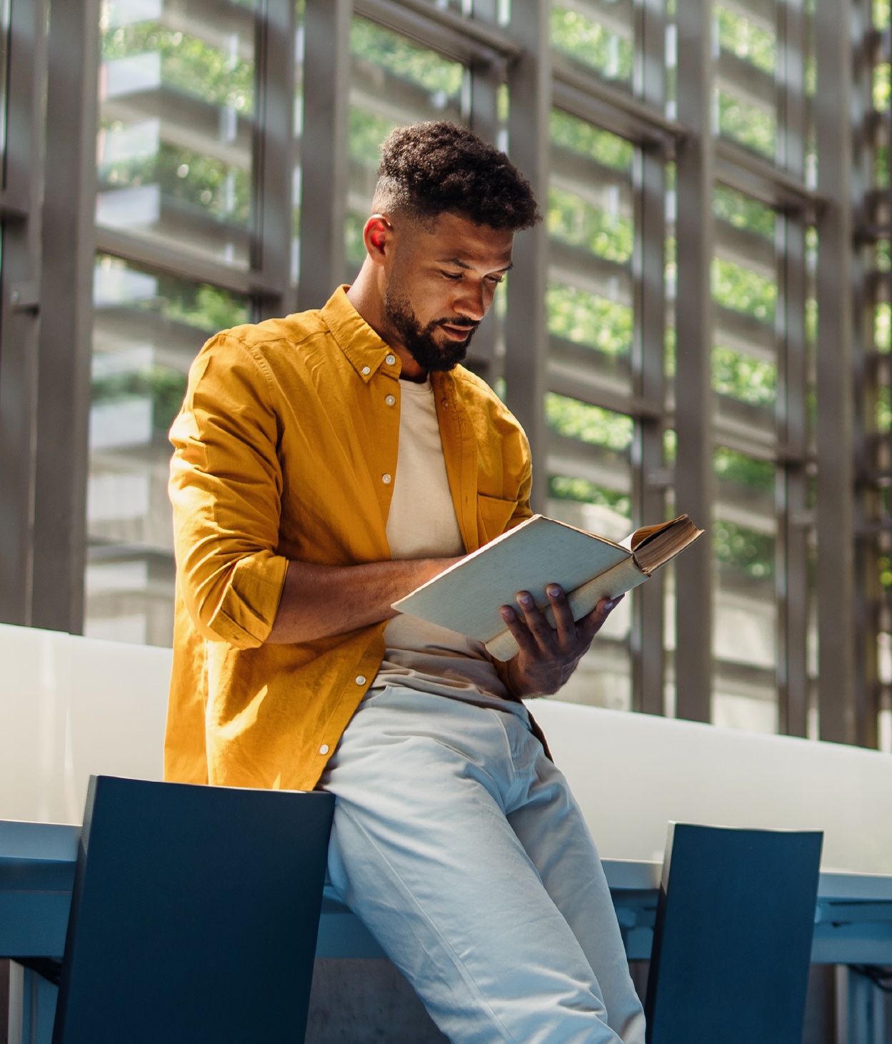 Giovane professionista di colore che legge un libro nell'atrio di un ufficio ben illuminato.